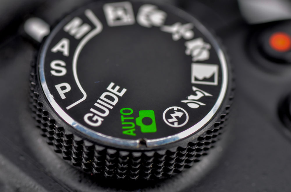 Close-up macro shot of a modern digital SLR camera. Detailed photo of black camera body with buttons to control and switch shooting modes. Selective focus.