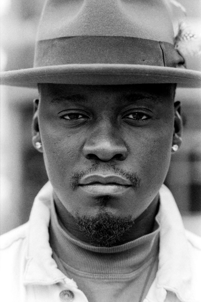 Head-shot of man wearing a hat and looking at camera in a black and white grainy portrait.