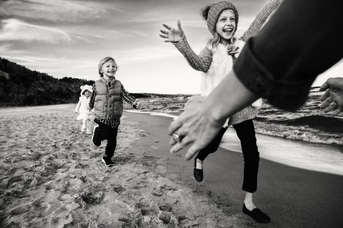 Group black and white portrait of three funny smiling laughing Caucasian children kids friends playing running to mother parent on ocean sea beach outdoors. Happy lifestyle childhood concept